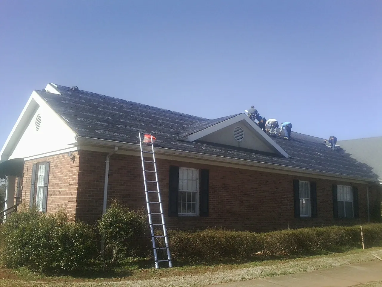 Crew tearing shingles off a brick ranch roof with a ladder set — Emergency Roof Repair work by our crew in Murrells Inlet