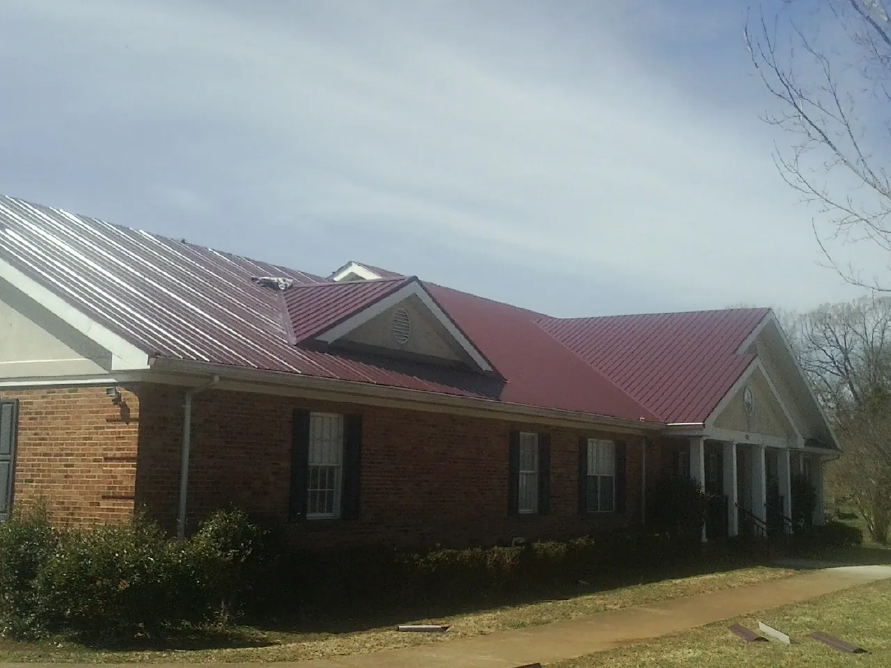 Red metal roof with gabled entries on a long brick building, from a Hail Damage Roof Repair job in Murrells Inlet