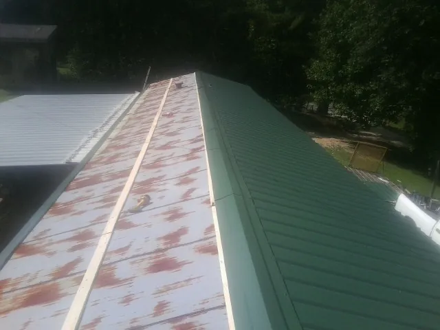 Old rusted panels beside newly installed green metal roofing — Wind Damage Roof Repair by Roofing Brothers in Murrells Inlet