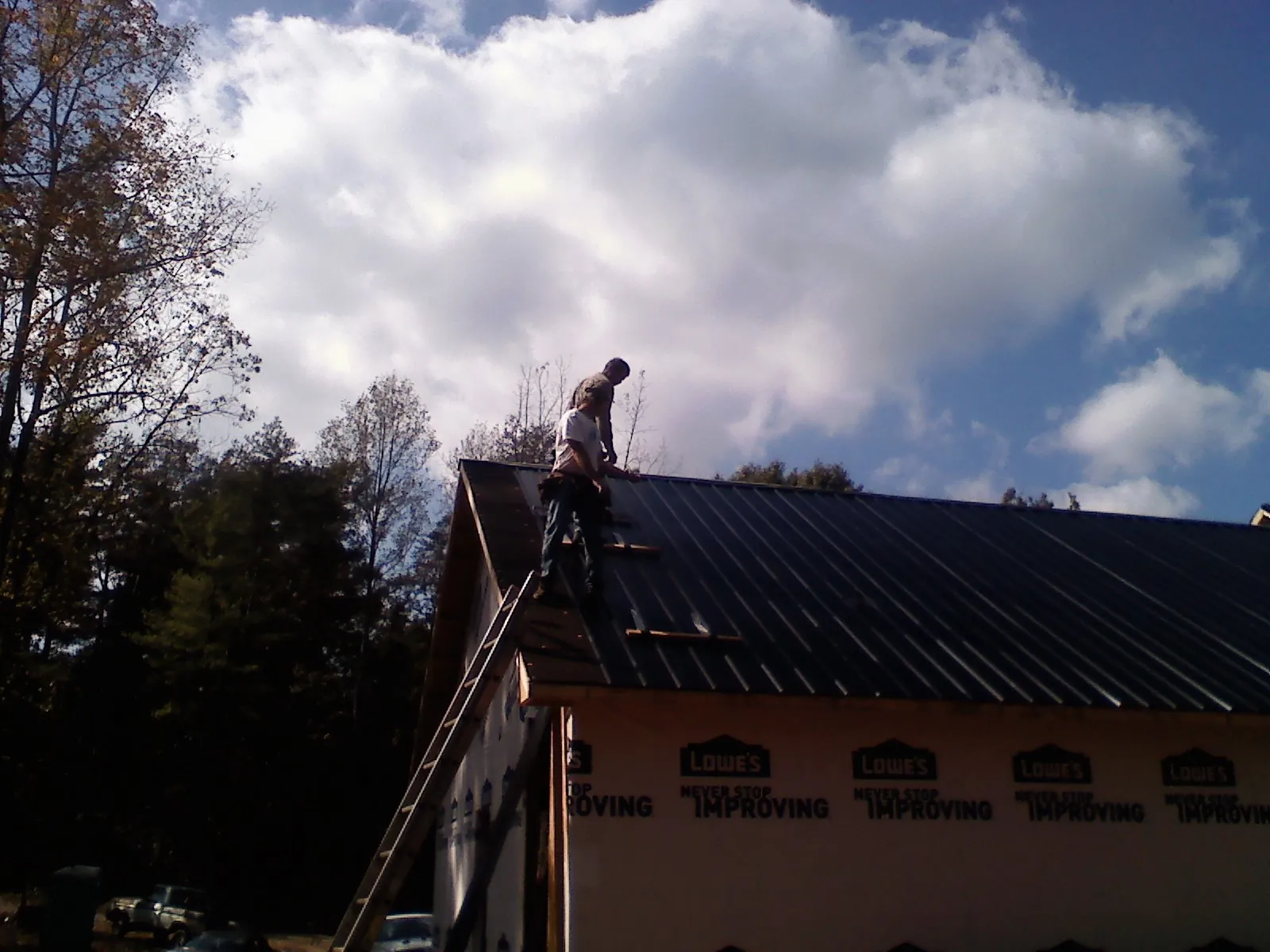 Roofer fastening dark metal panels high against a cloudy sky, from a Roof Inspection job in Murrells Inlet
